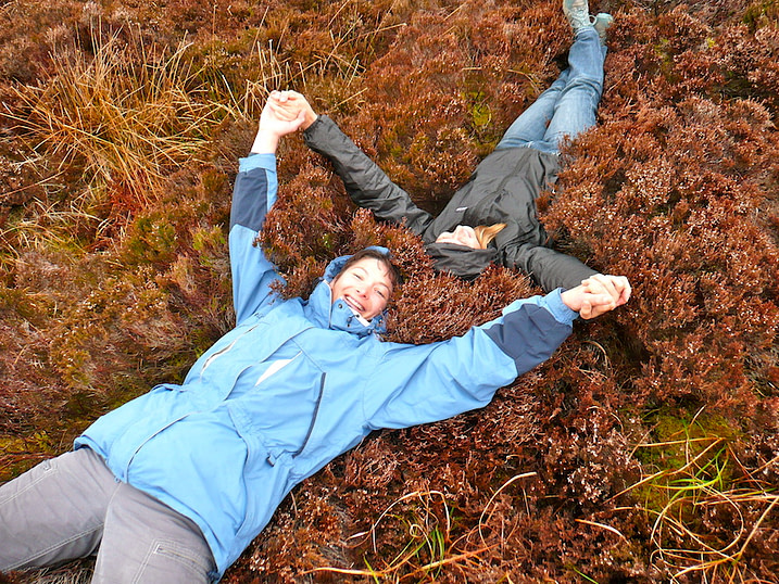 Two women holding hands lying down in heather